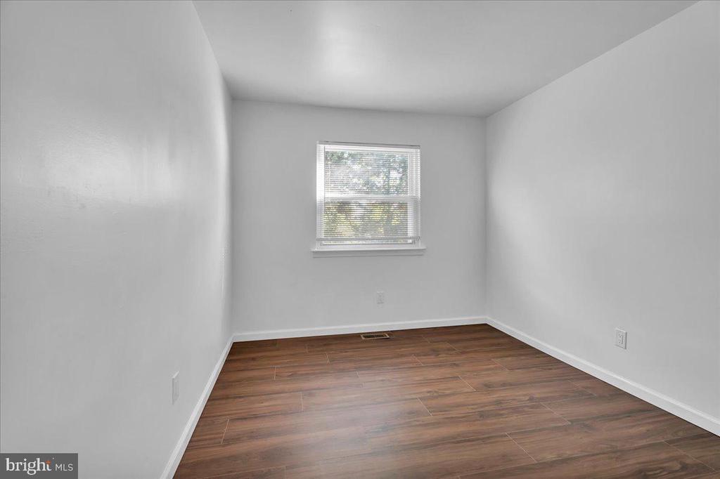 Empty room with brown plank flooring, white walls, and a window with blinds.