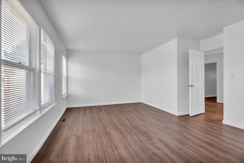 Empty room with brown wood-look flooring, white walls, and windows with blinds.