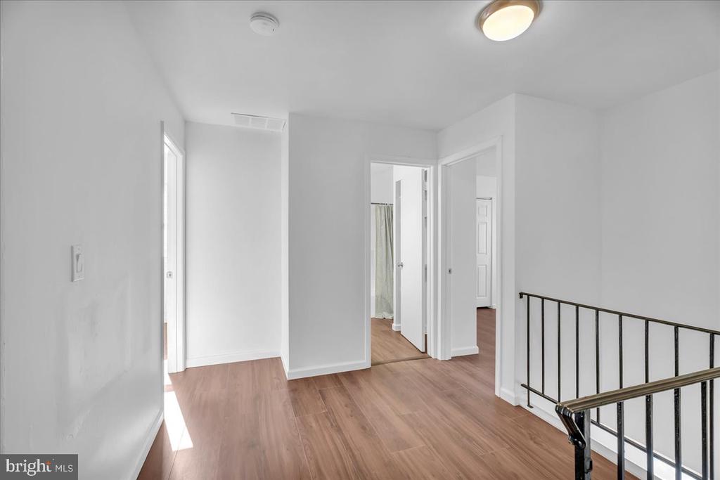 Upstairs hallway with wood-look floors, open doorways, and a black metal stair railing.