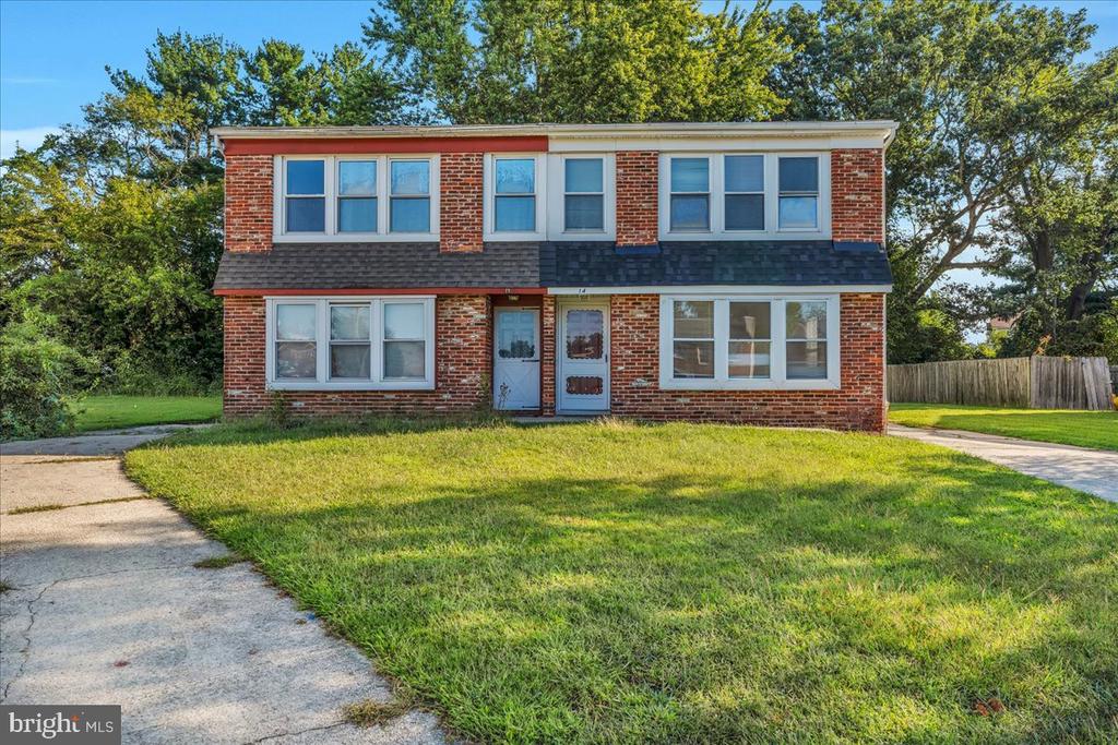 Two-story brick home with paired front entrances, a broad lawn, and mature trees.