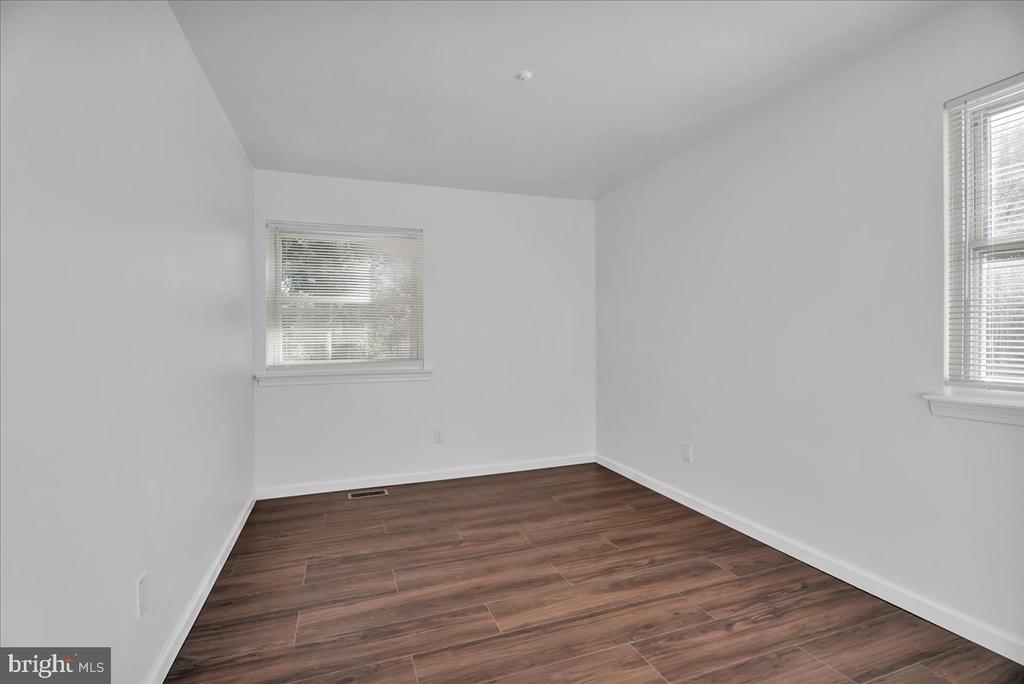 Empty room with white walls, two windows with blinds, and dark wood-look plank flooring.