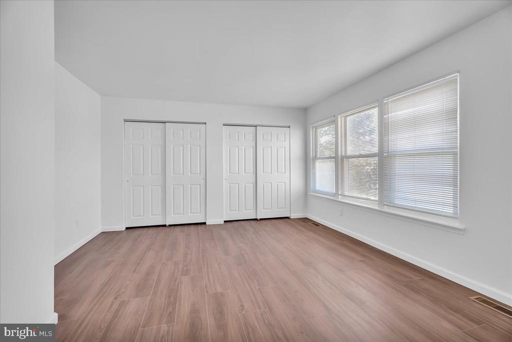 Empty room with wood-look floors, two closets, and large windows with blinds.