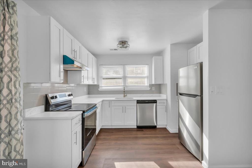 Kitchen with white cabinets, stainless steel appliances, dark counters, and a wide window above the sink.