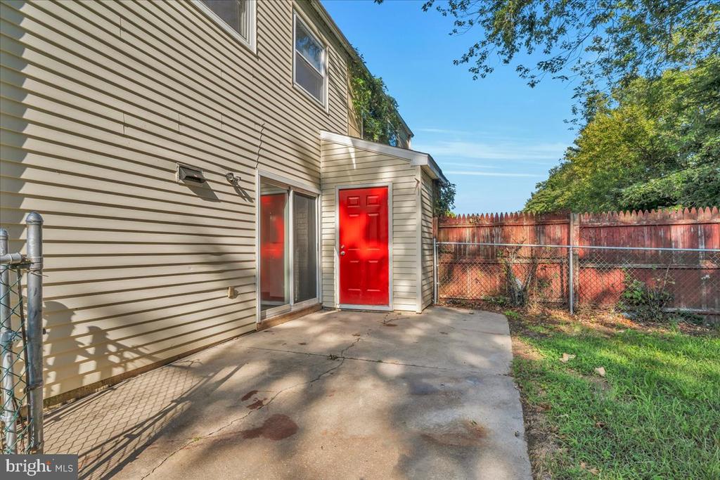 Concrete patio beside a house, featuring a bright red rear door and fenced yard.