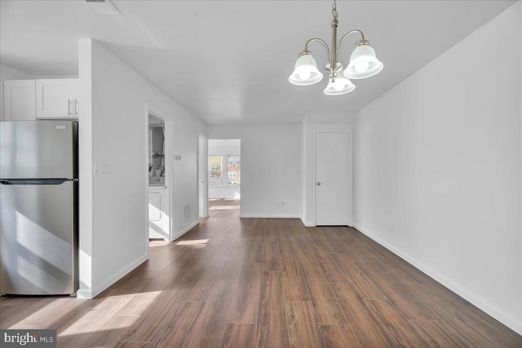Empty dining area with wood-look flooring, a chandelier, and a stainless-steel refrigerator at left.