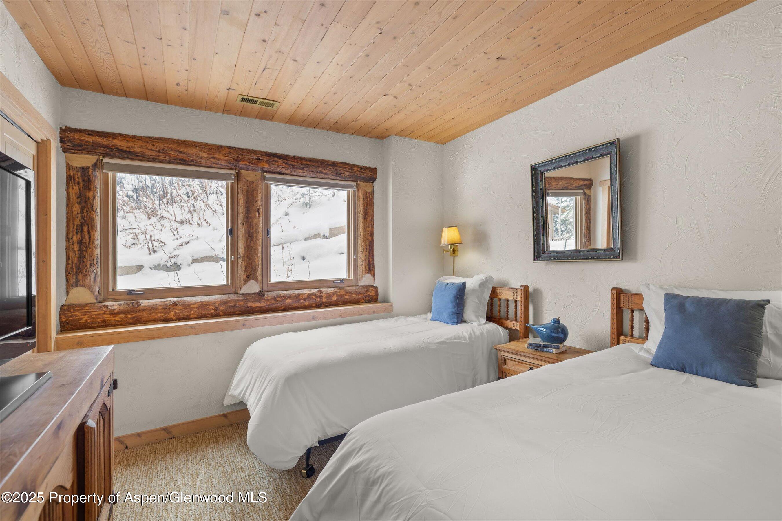 Twin bedroom with rustic log-trimmed windows overlooking snow-covered ground.