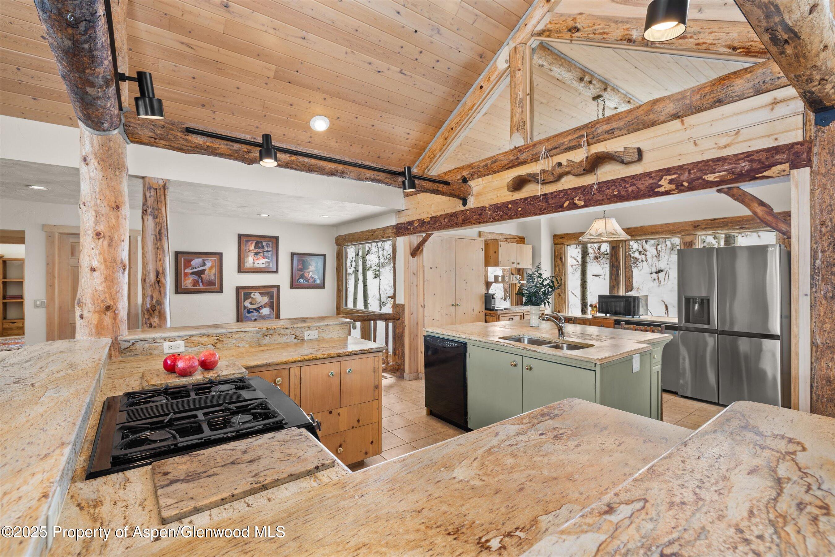 Rustic kitchen with exposed log beams, stone counters, pale green island, and snowy views through the windows.
