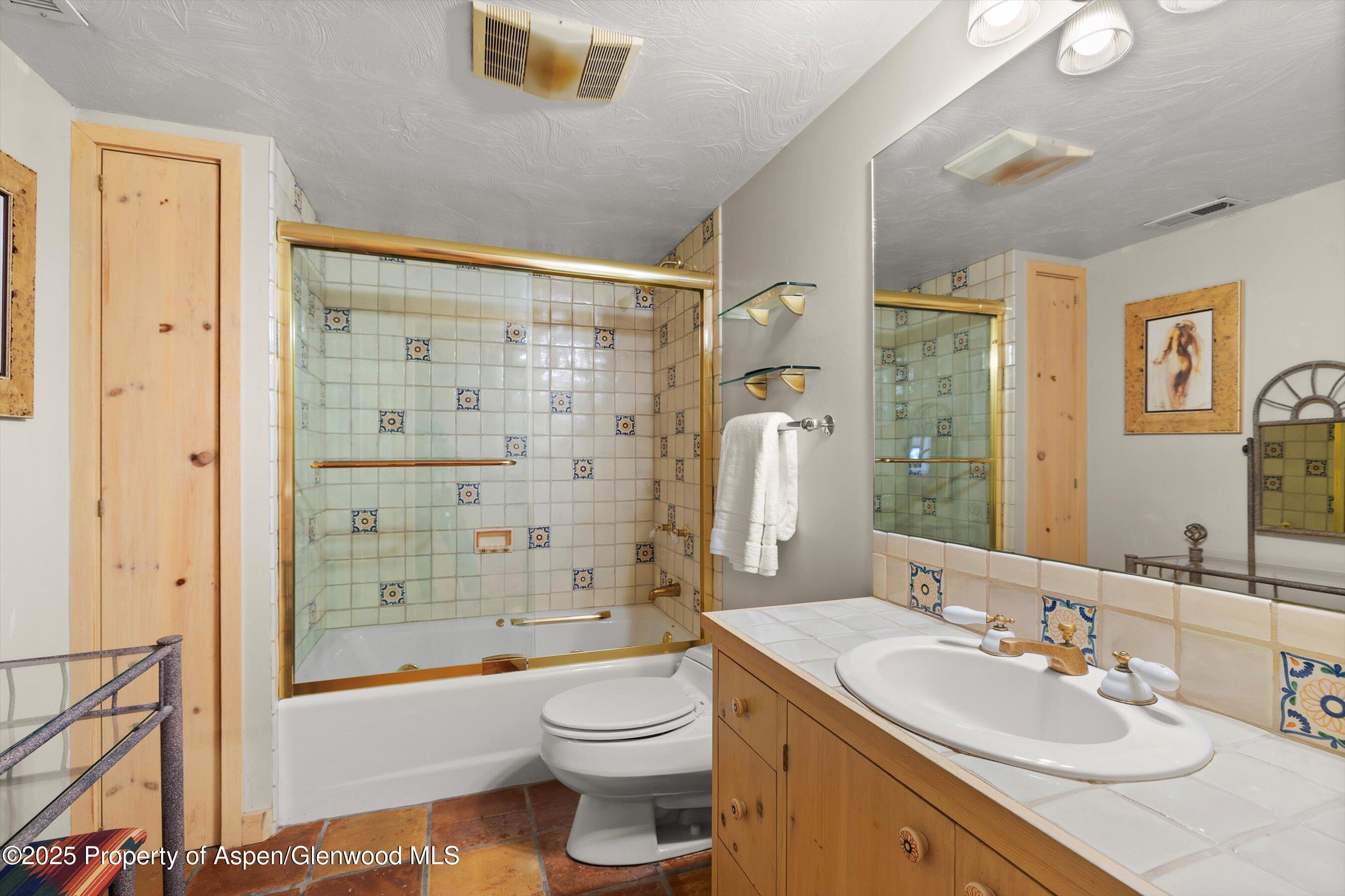 Bathroom with a tiled tub and shower, patterned accent tiles, and a wood vanity with an oval sink.