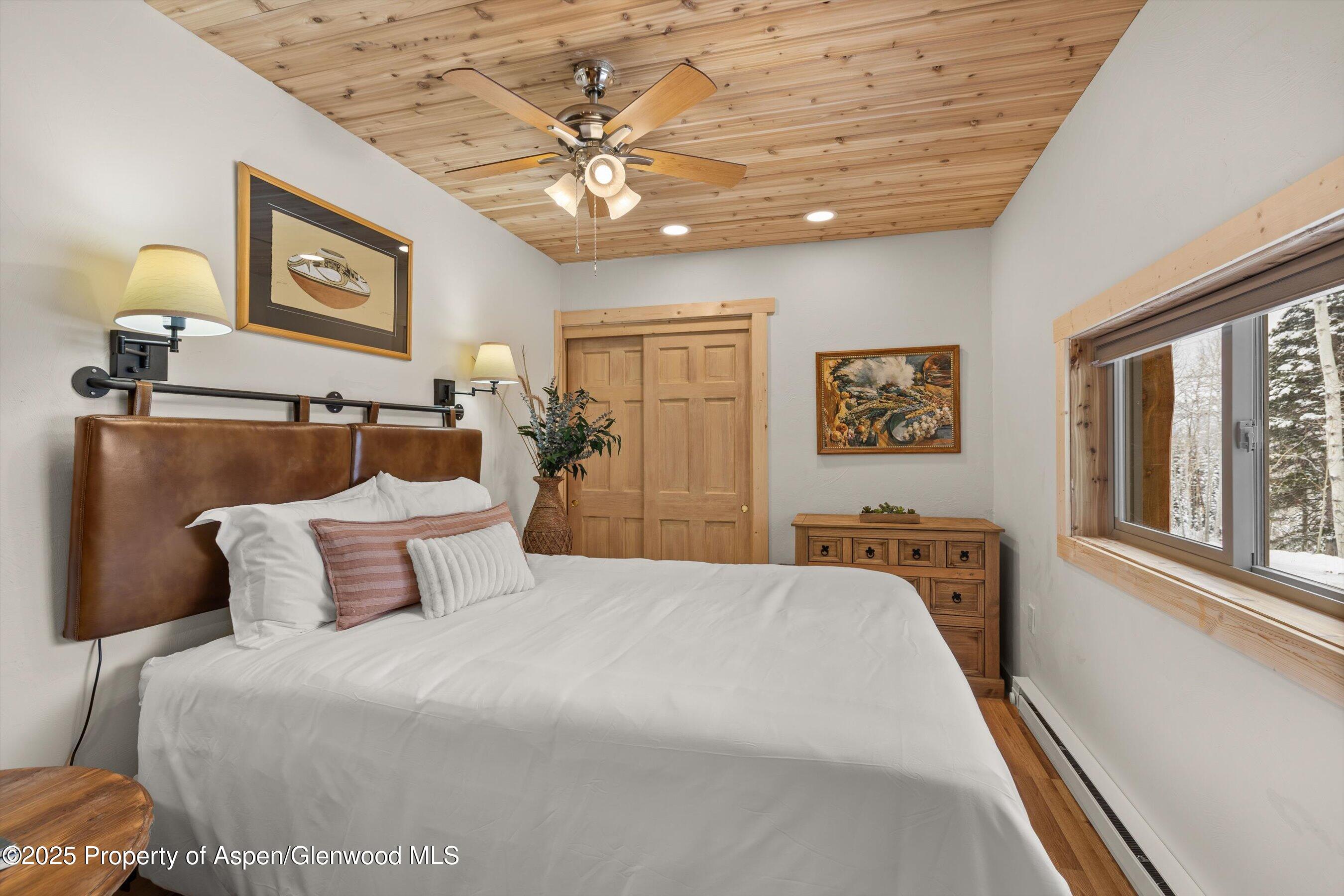 Bedroom with a wood-plank ceiling, leather headboard, and snowy trees visible through the window.