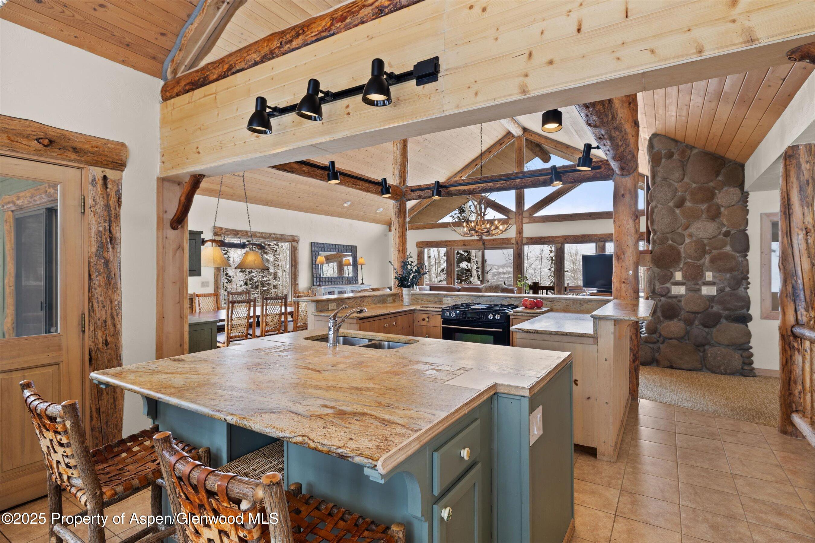 Rustic kitchen with a broad stone island, exposed timber beams, and a rounded-stone fireplace.