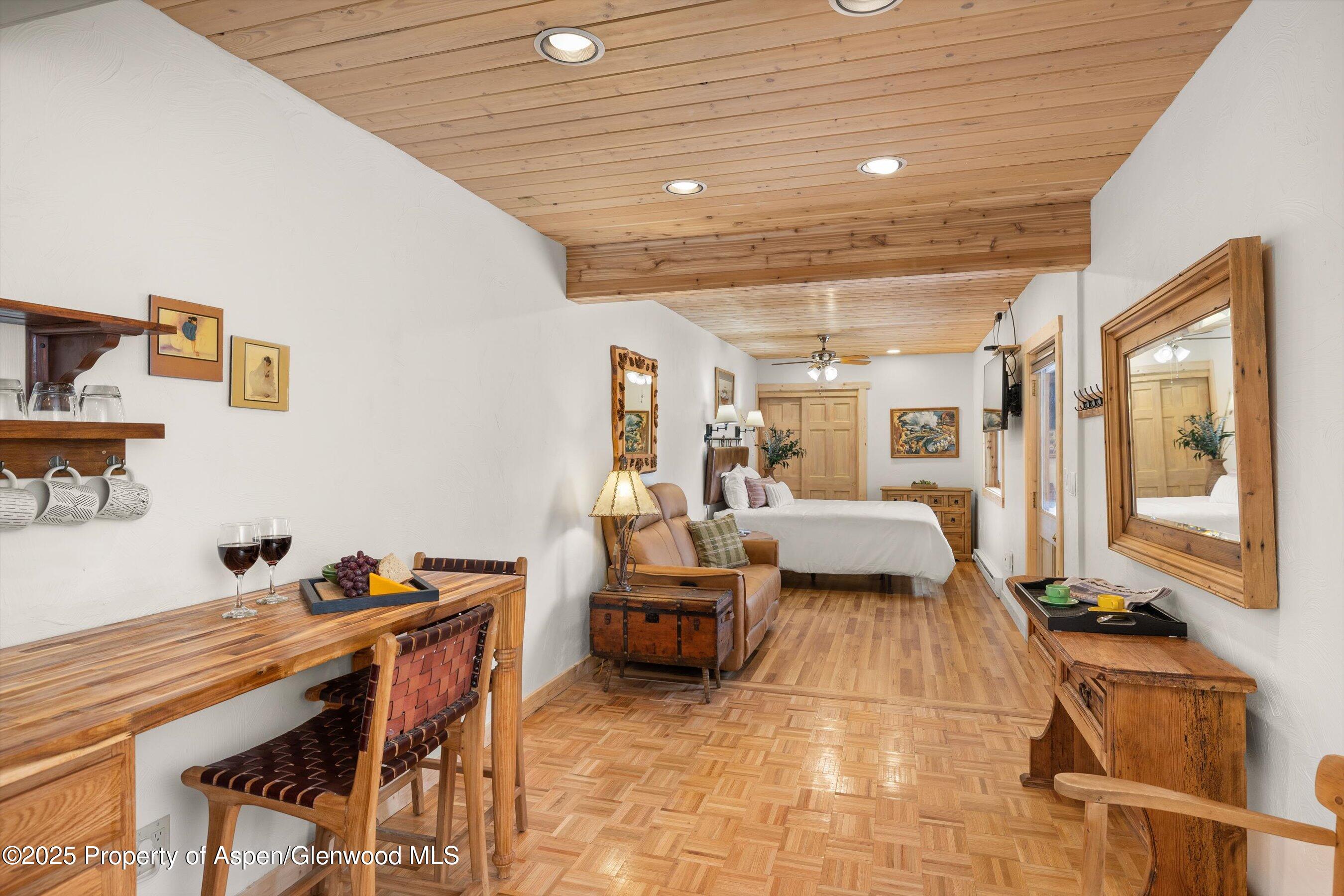 Furnished bedroom suite with a wood-plank ceiling, parquet floor, and dining table.