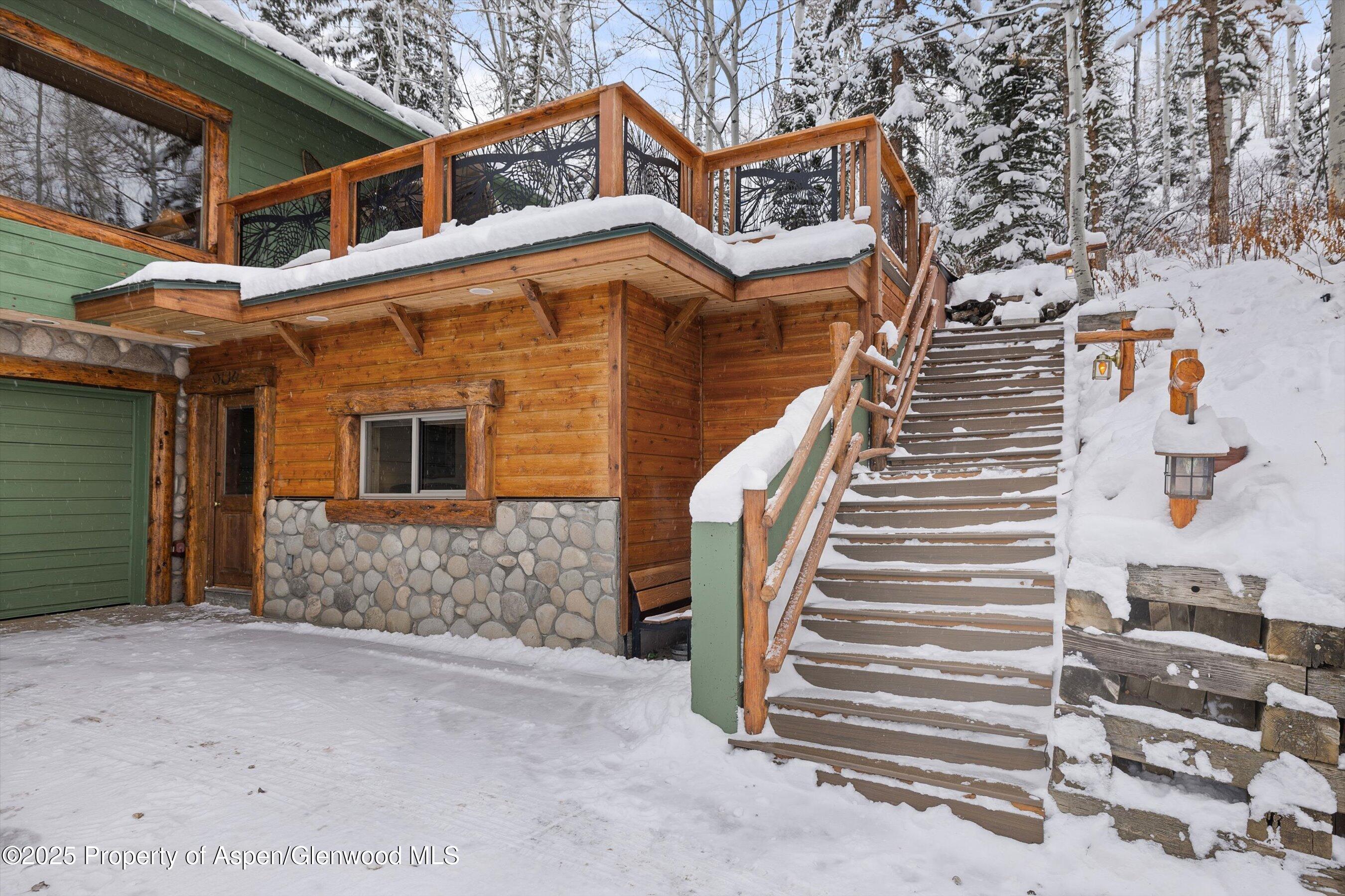 Mountain home with a snow-covered timber staircase, raised deck, and wood-and-stone facade.