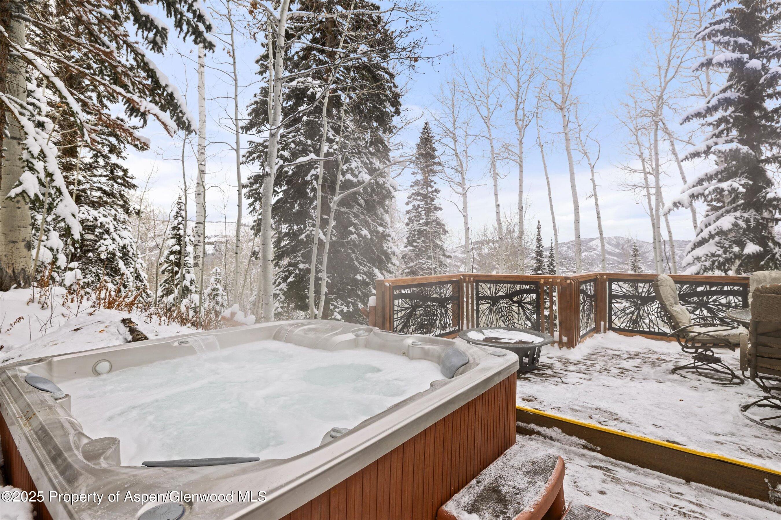 Outdoor hot tub on a snowy deck, surrounded by trees with mountain views.