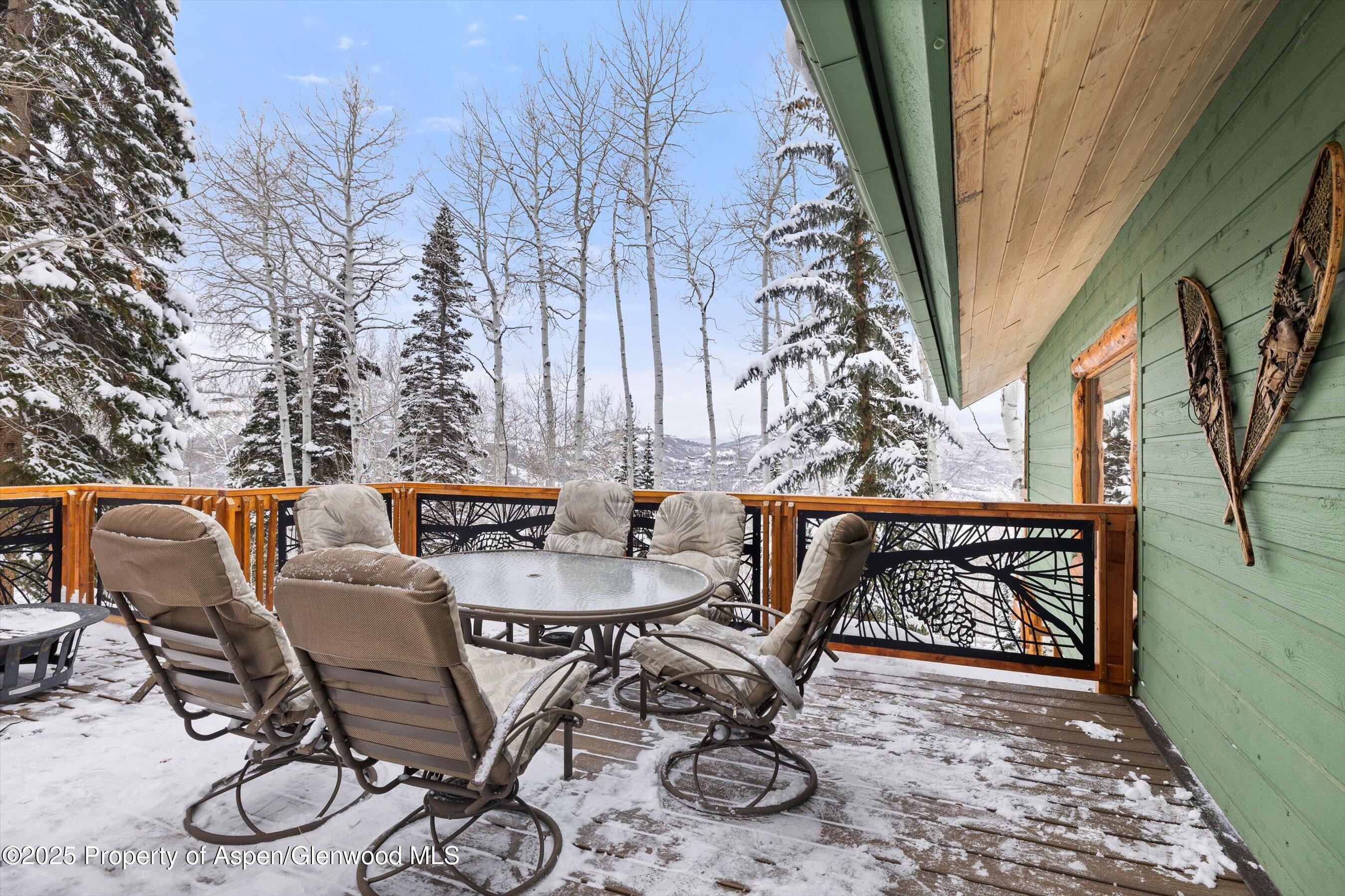 Snow-dusted deck with patio dining set, decorative railing, and a snowy mountain view.