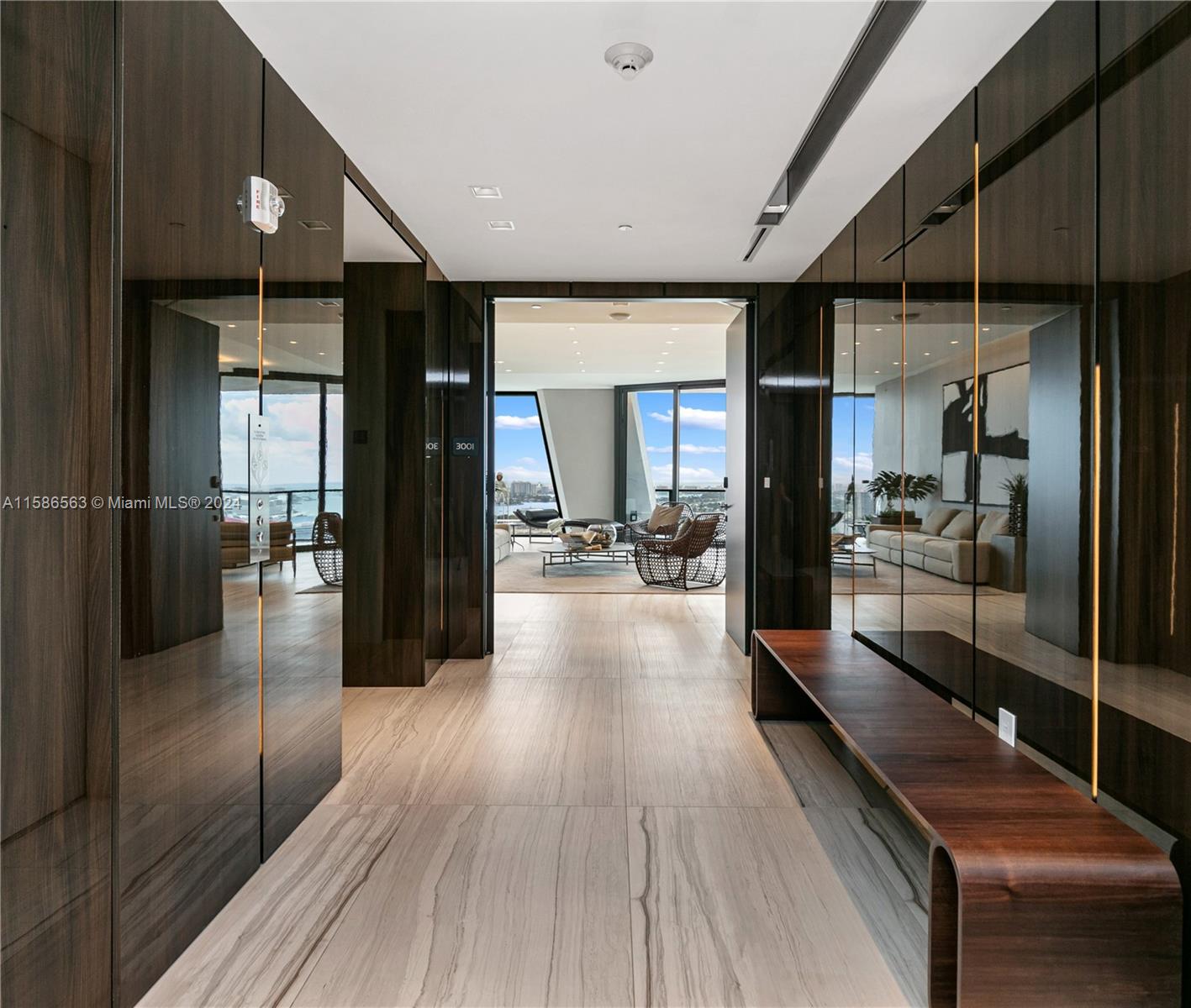 Modern condo foyer with dark mirrored walls, a stone floor, and a bright living area beyond.