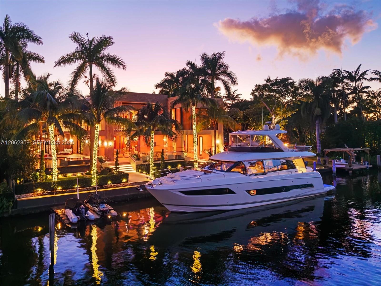 Modern waterfront home and docked yacht framed by palms at dusk.