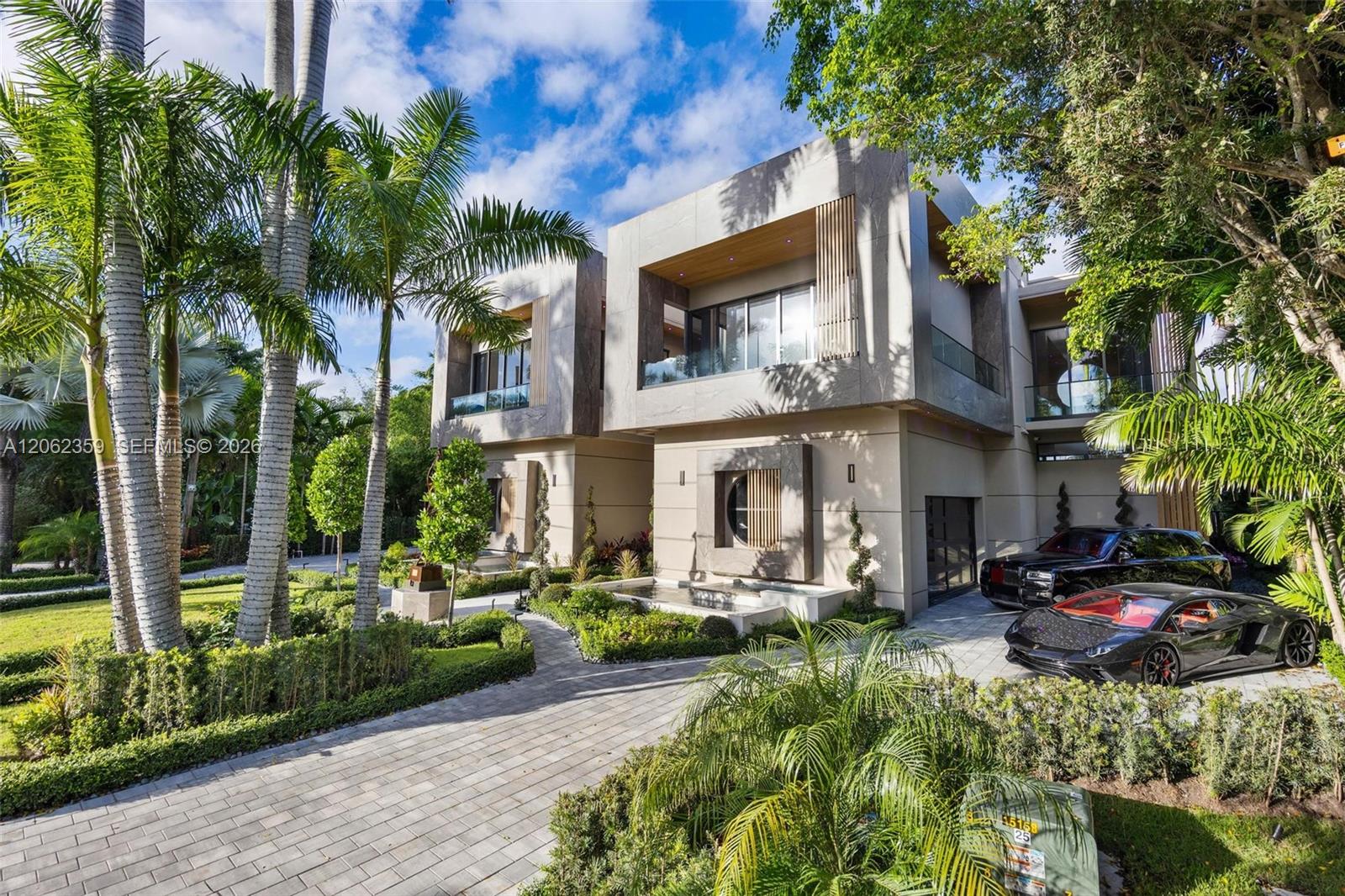 Modern two-story home with a pale stone facade, tropical landscaping, and cars in the driveway.