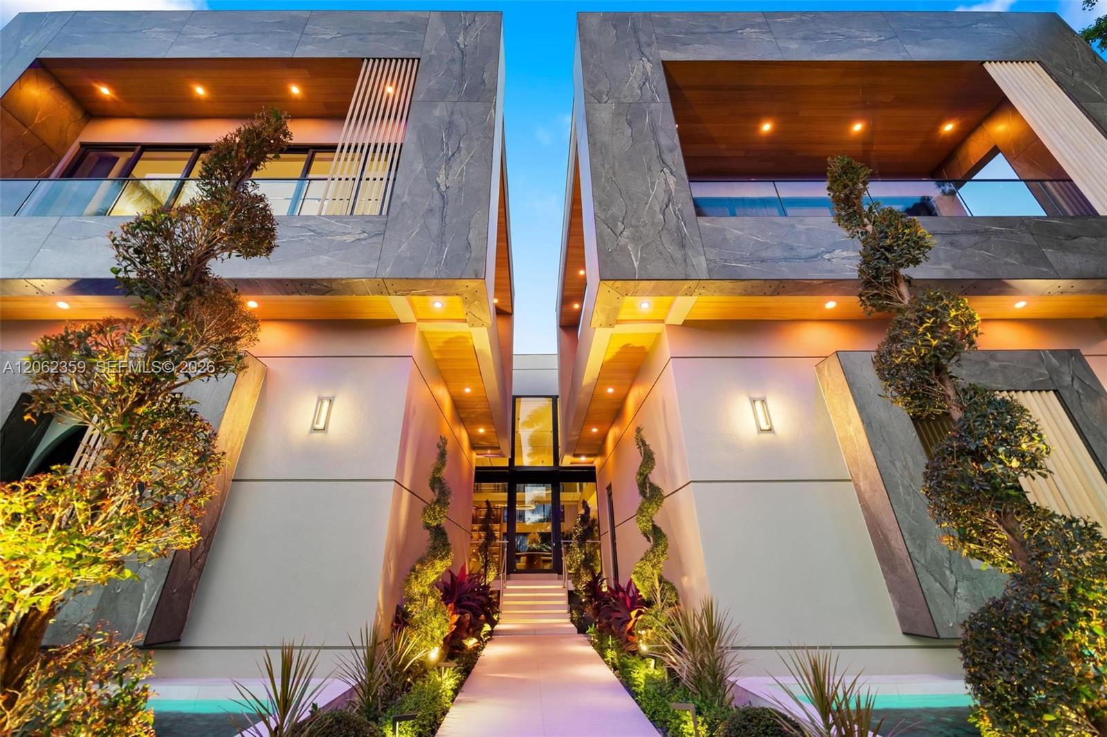 Modern home entrance framed by gray stone, warm wood soffits, landscaped paths, and reflecting pools.