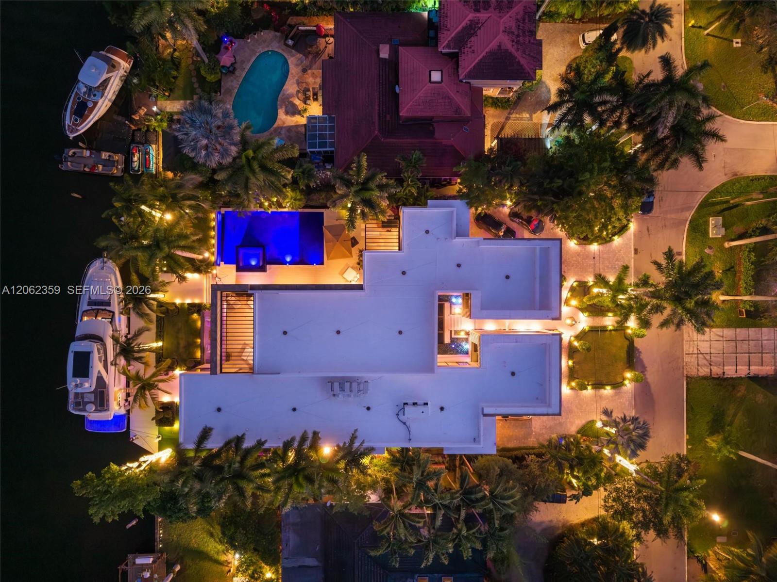 Aerial view of a waterfront home with a bright pool and boats docked beside it.