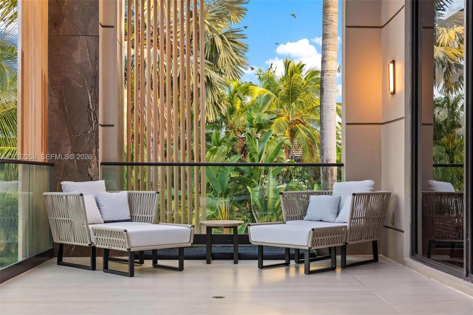 Furnished balcony with cushioned lounge chairs overlooking tropical palms.