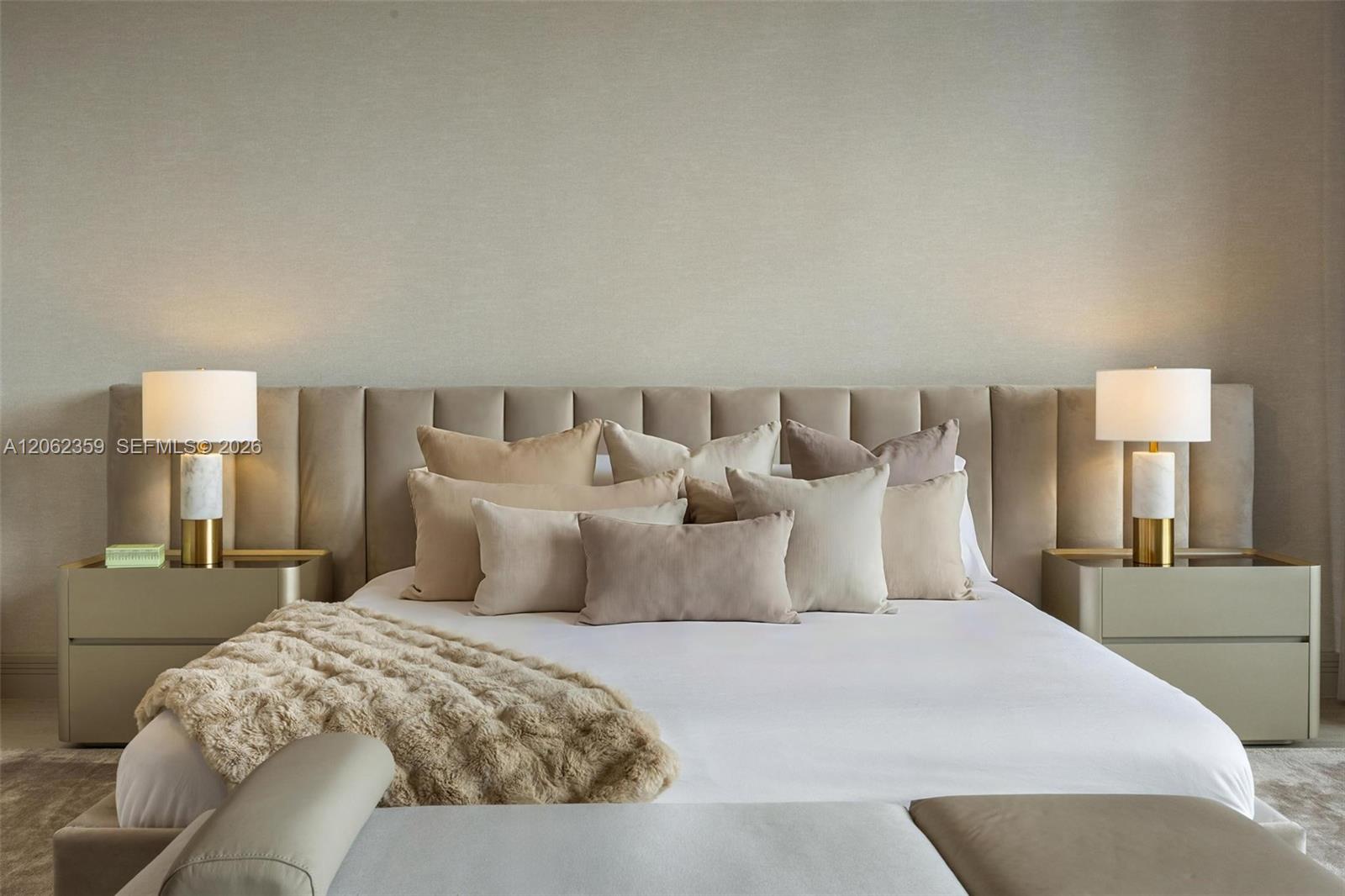 Neutral bedroom with a white bed, tall upholstered headboard, matching bedside tables, and lamps.