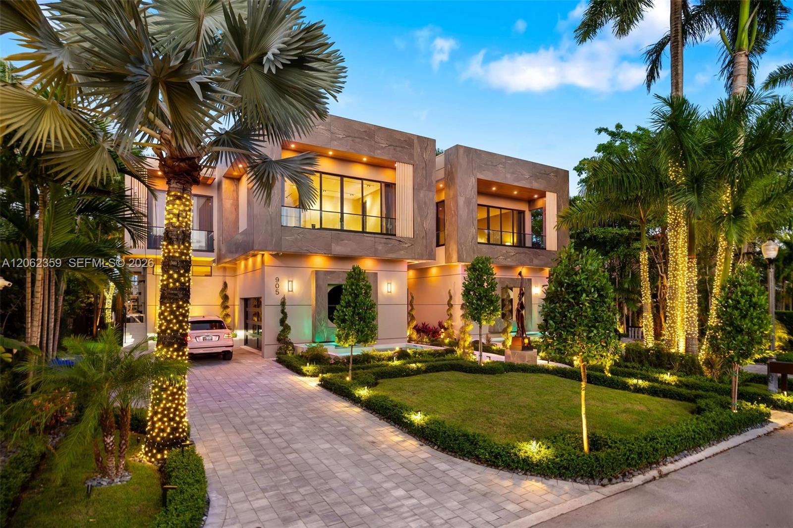 Modern two-story home with stone facade, illuminated palms, and landscaped driveway at dusk.