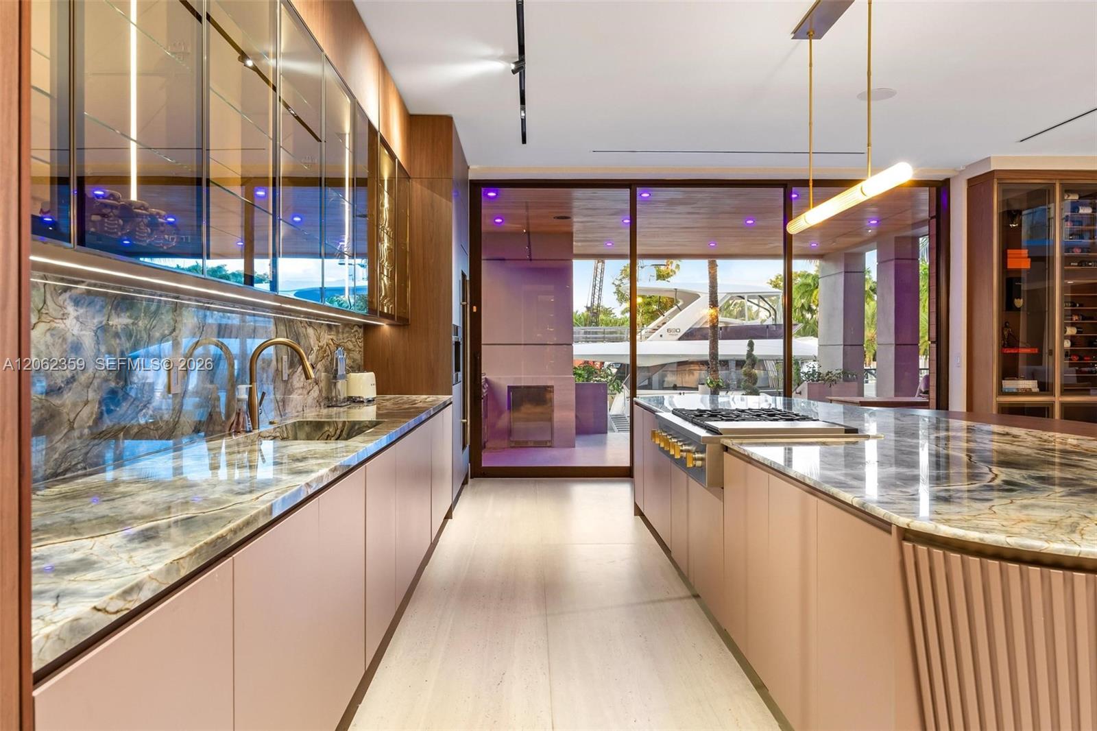 Modern kitchen with marble counters, wood cabinetry, a large cooktop island, and a yacht visible through glass doors.