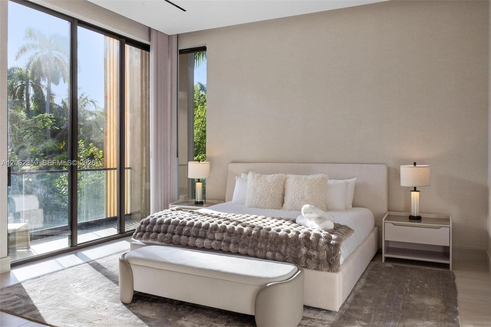 Modern bedroom with an upholstered bed and floor-to-ceiling windows overlooking tropical greenery.