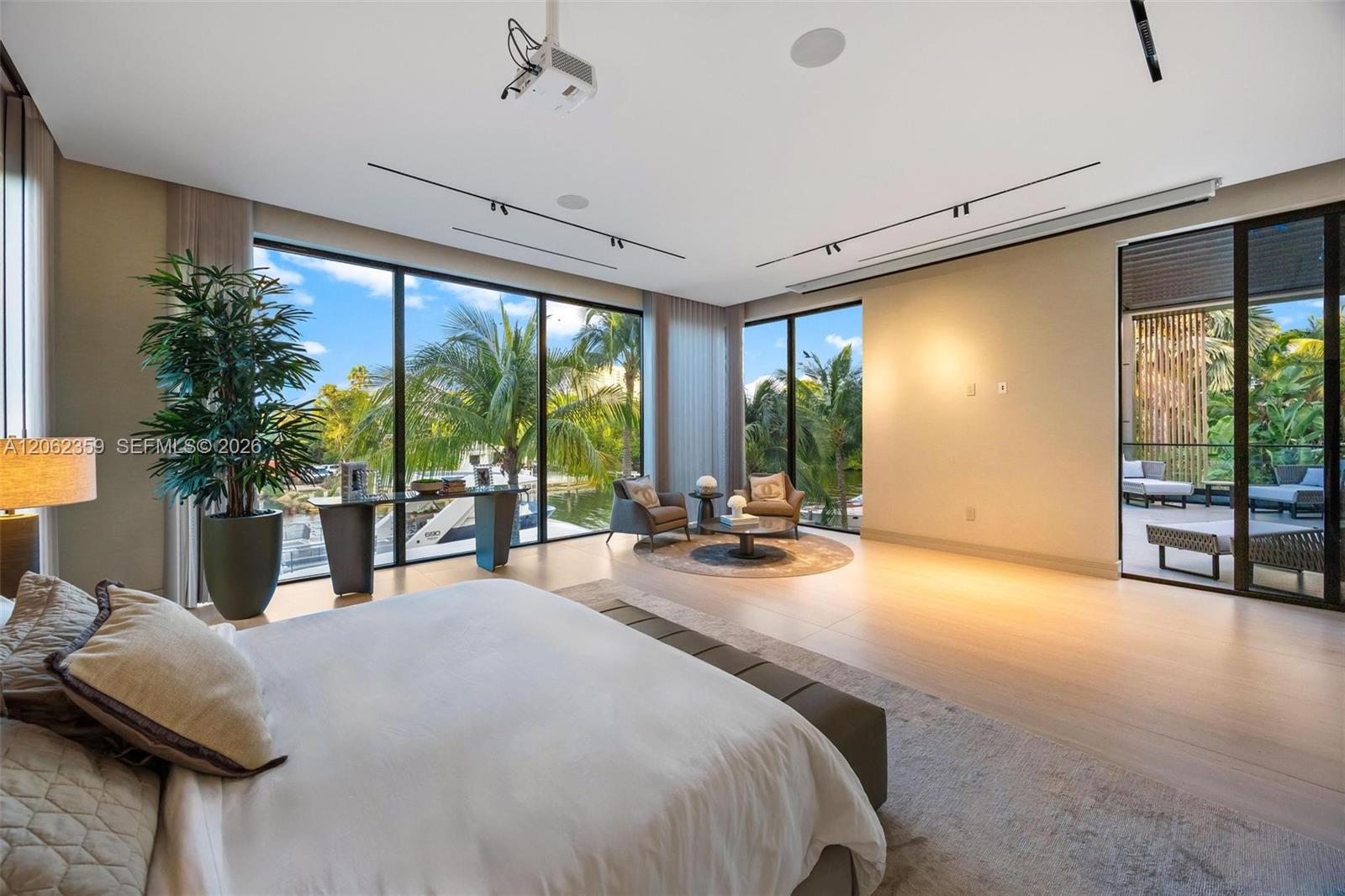Furnished bedroom with floor-to-ceiling windows overlooking palms, water, and a boat.