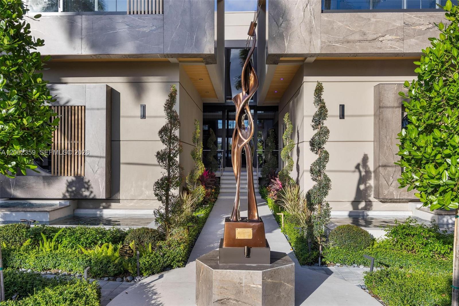 Modern home entrance with a tall bronze sculpture centered along the landscaped walkway.