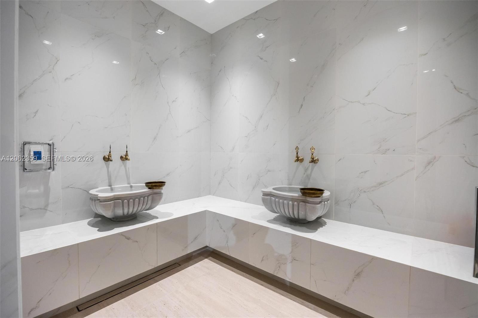 Bathroom with two sculptural white sinks, an L-shaped marble counter, and brass faucets.