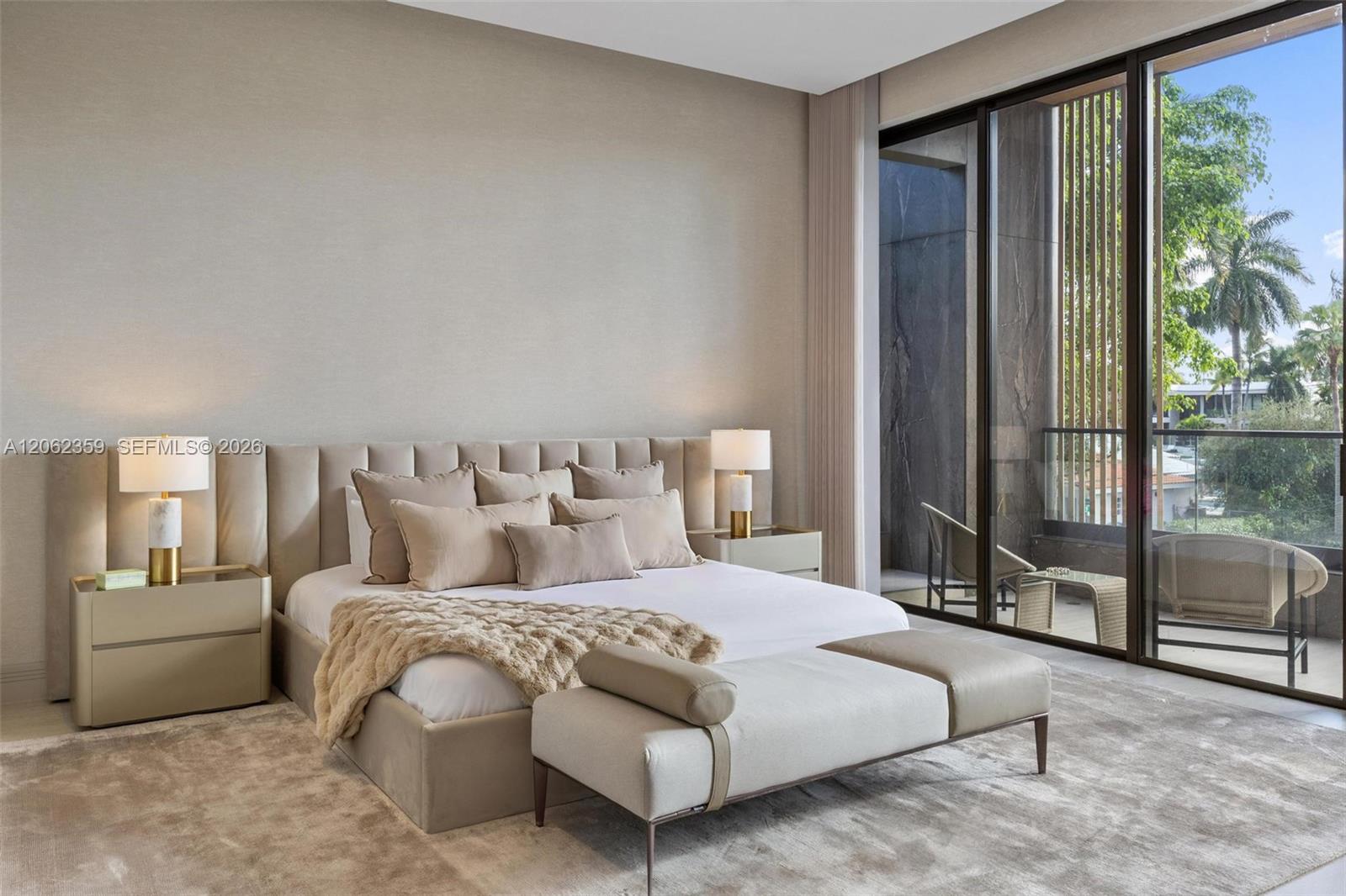 Modern bedroom with a neutral upholstered bed and floor-to-ceiling doors opening to a furnished balcony.