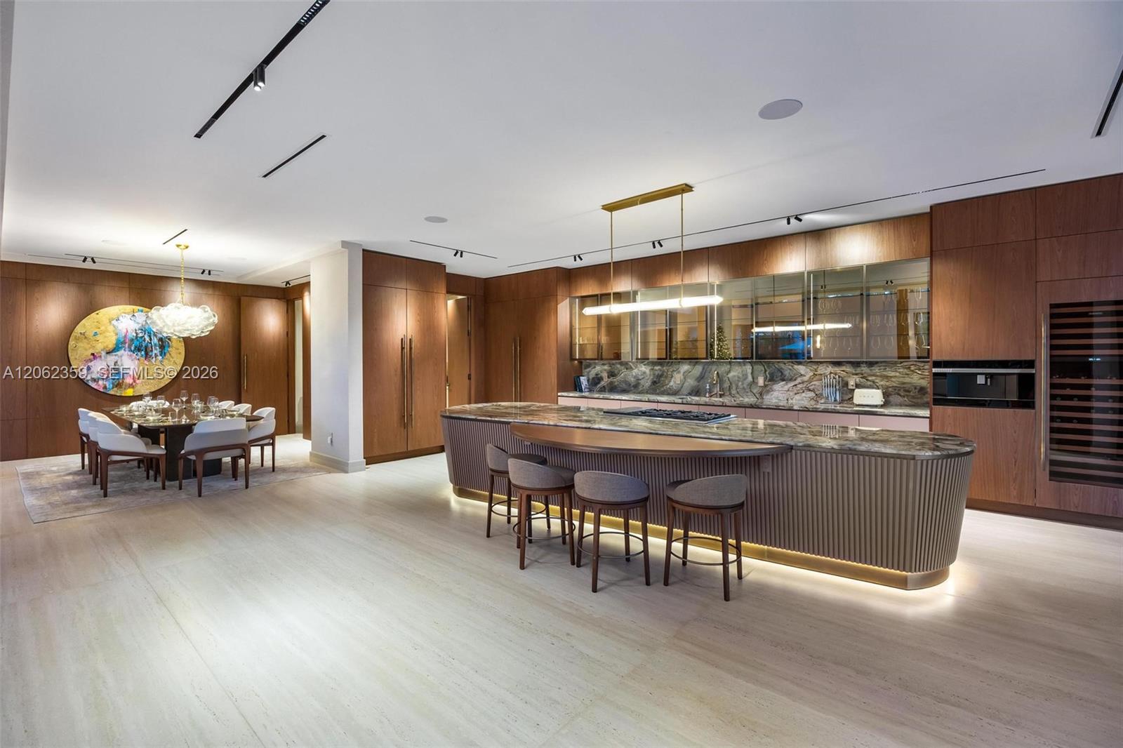 Modern kitchen with a large curved stone island, wood cabinetry, and an adjoining dining area.