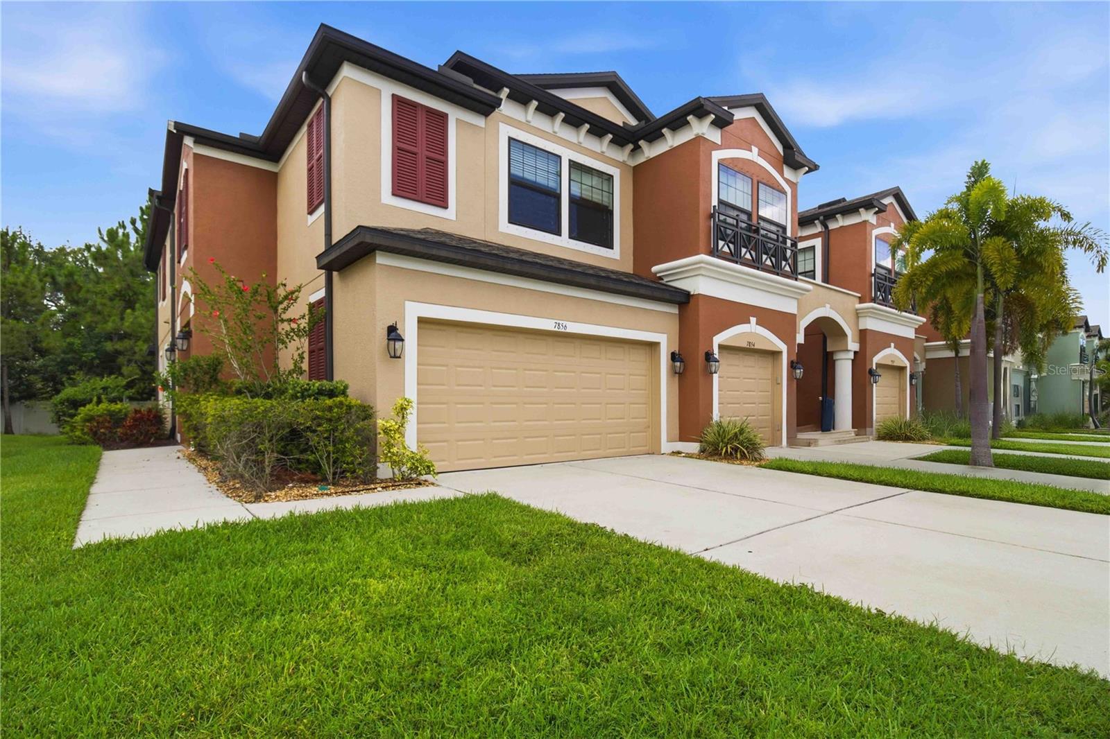 Attached townhomes with terracotta accents, balconies, and garages along a palm-lined street.