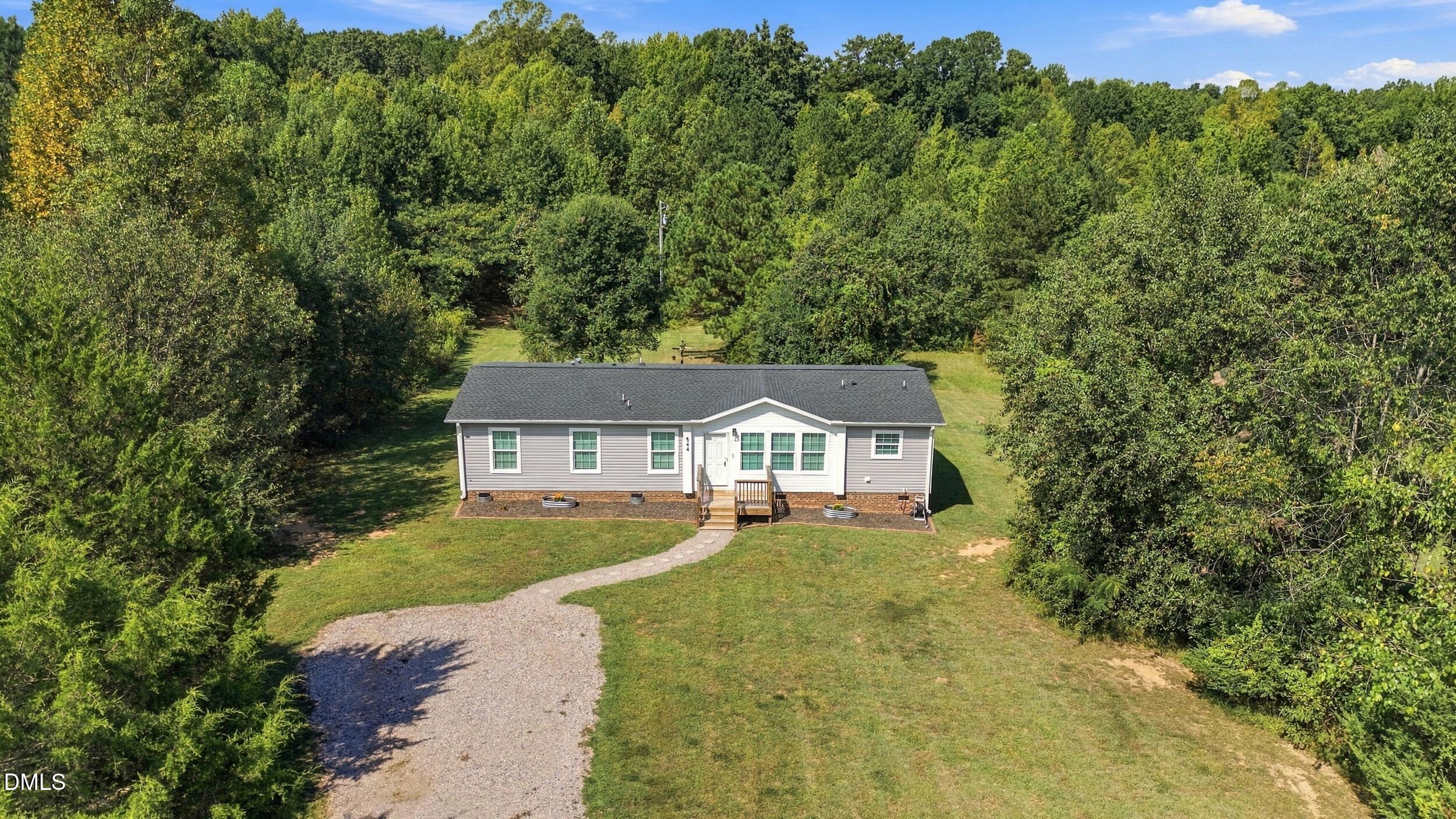 Single-story home with a front porch and curved gravel driveway, surrounded by dense trees.