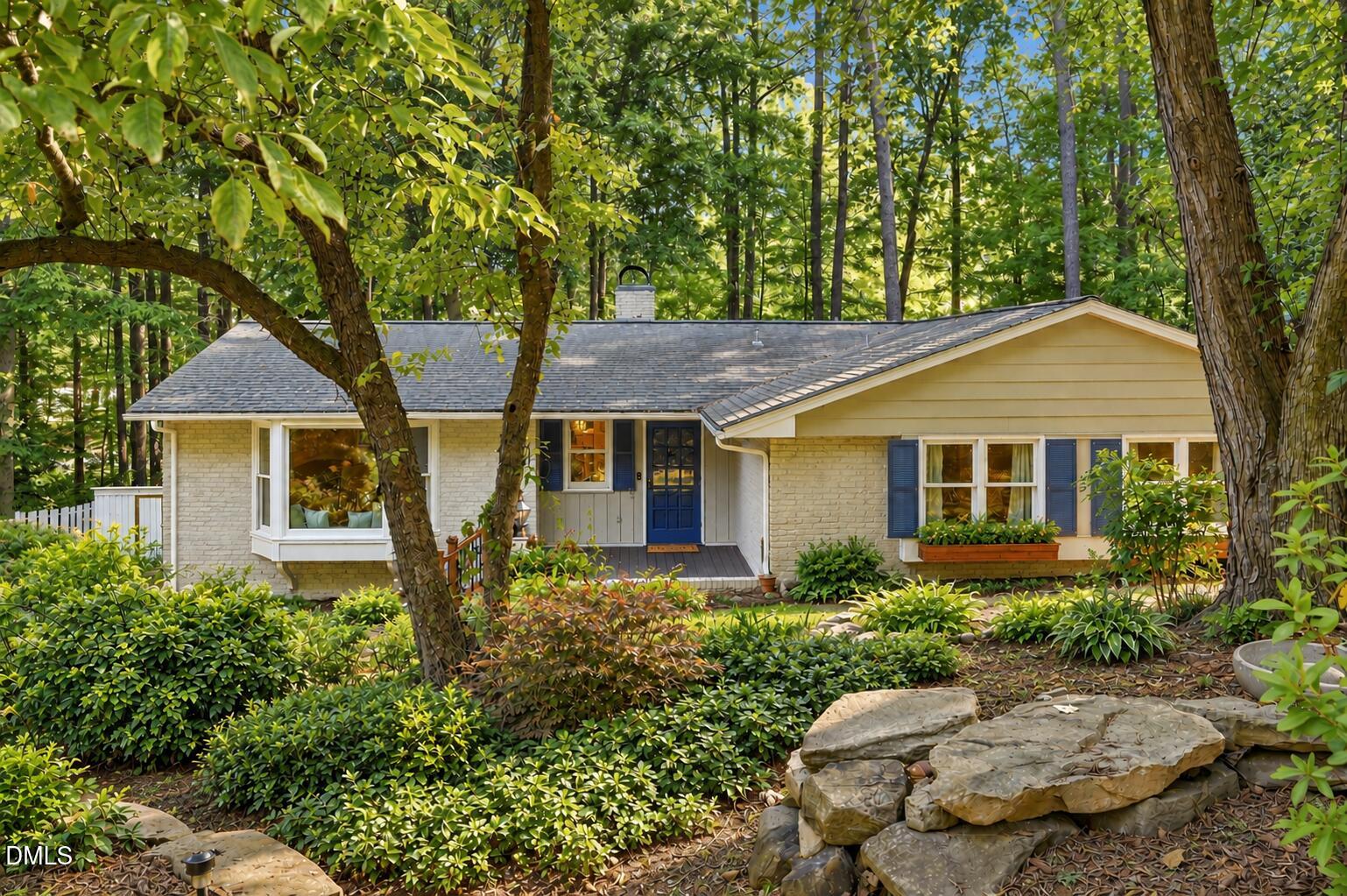 Single-story home nestled among mature trees, with a blue front door and landscaped stone feature.