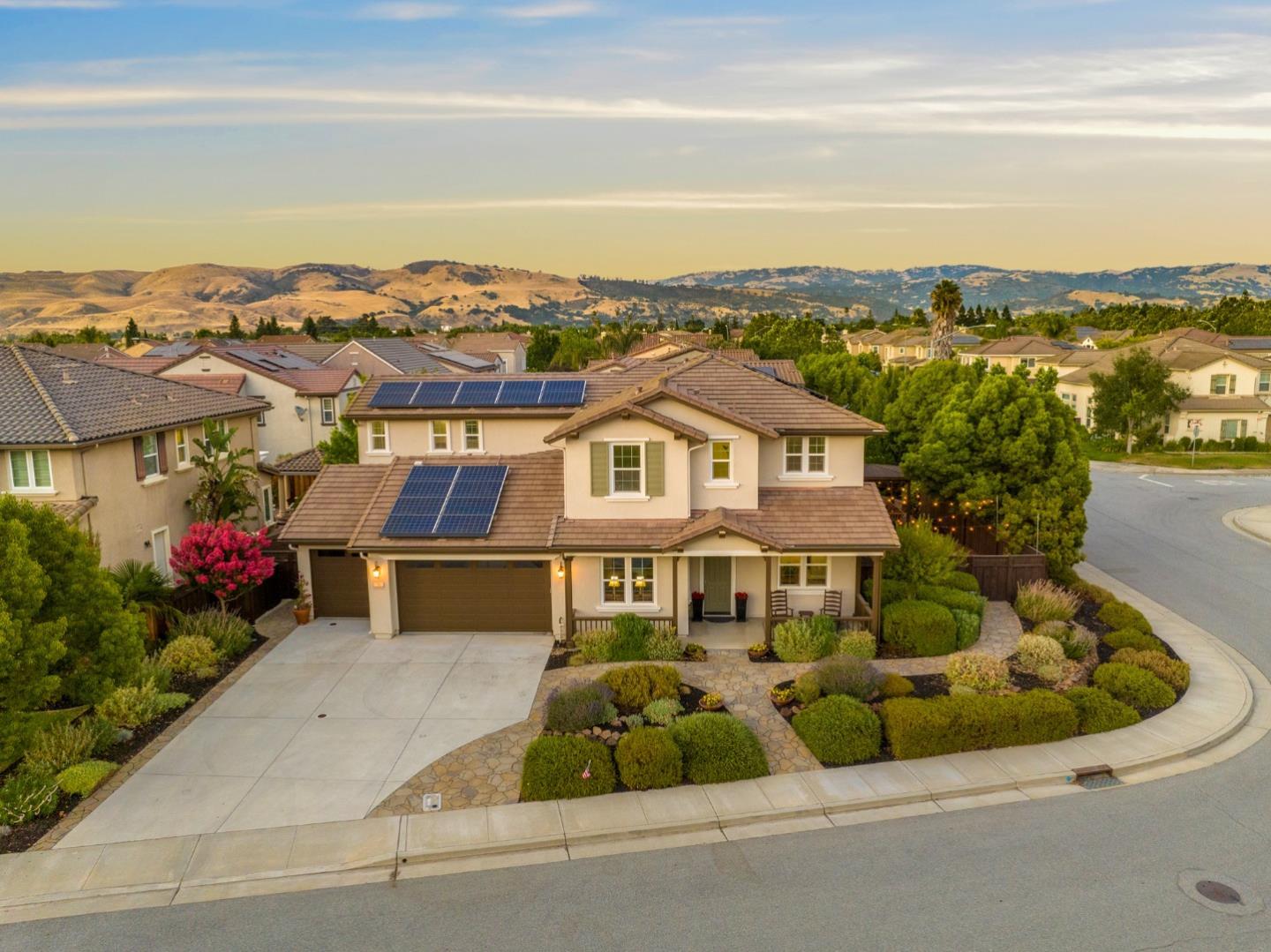 Two-story home with rooftop solar panels, landscaped yard, and rolling hills beyond.