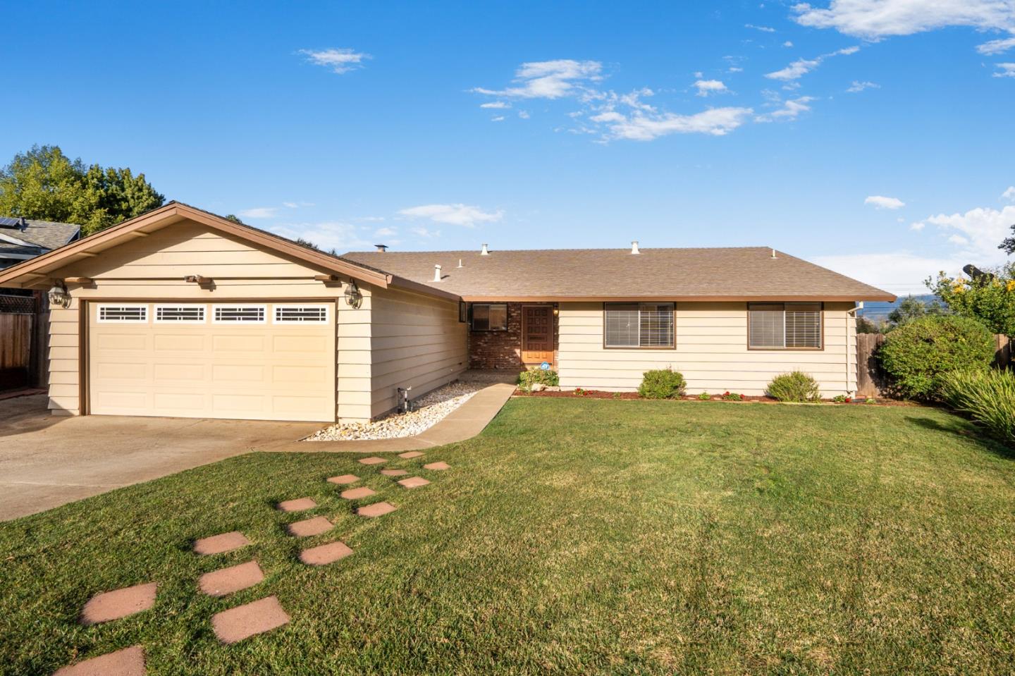 Single-story beige home with an attached garage and stepping stones across the front lawn.