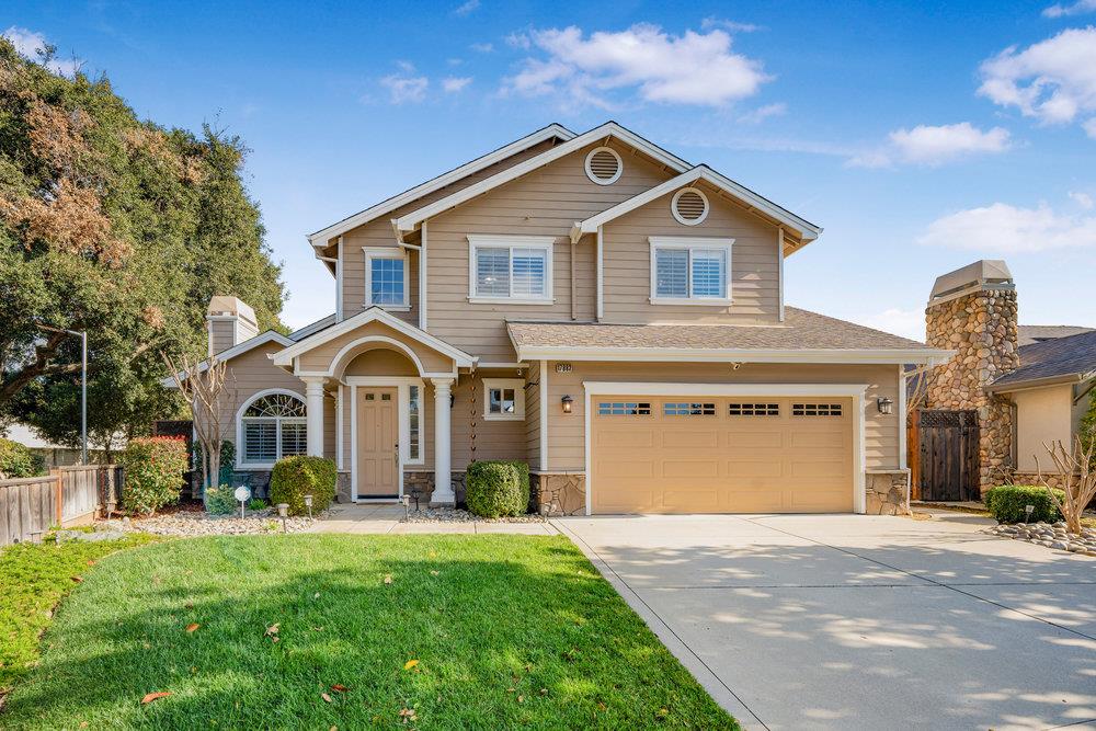 Two-story beige house with a covered entry, two-car garage, and stone chimney.