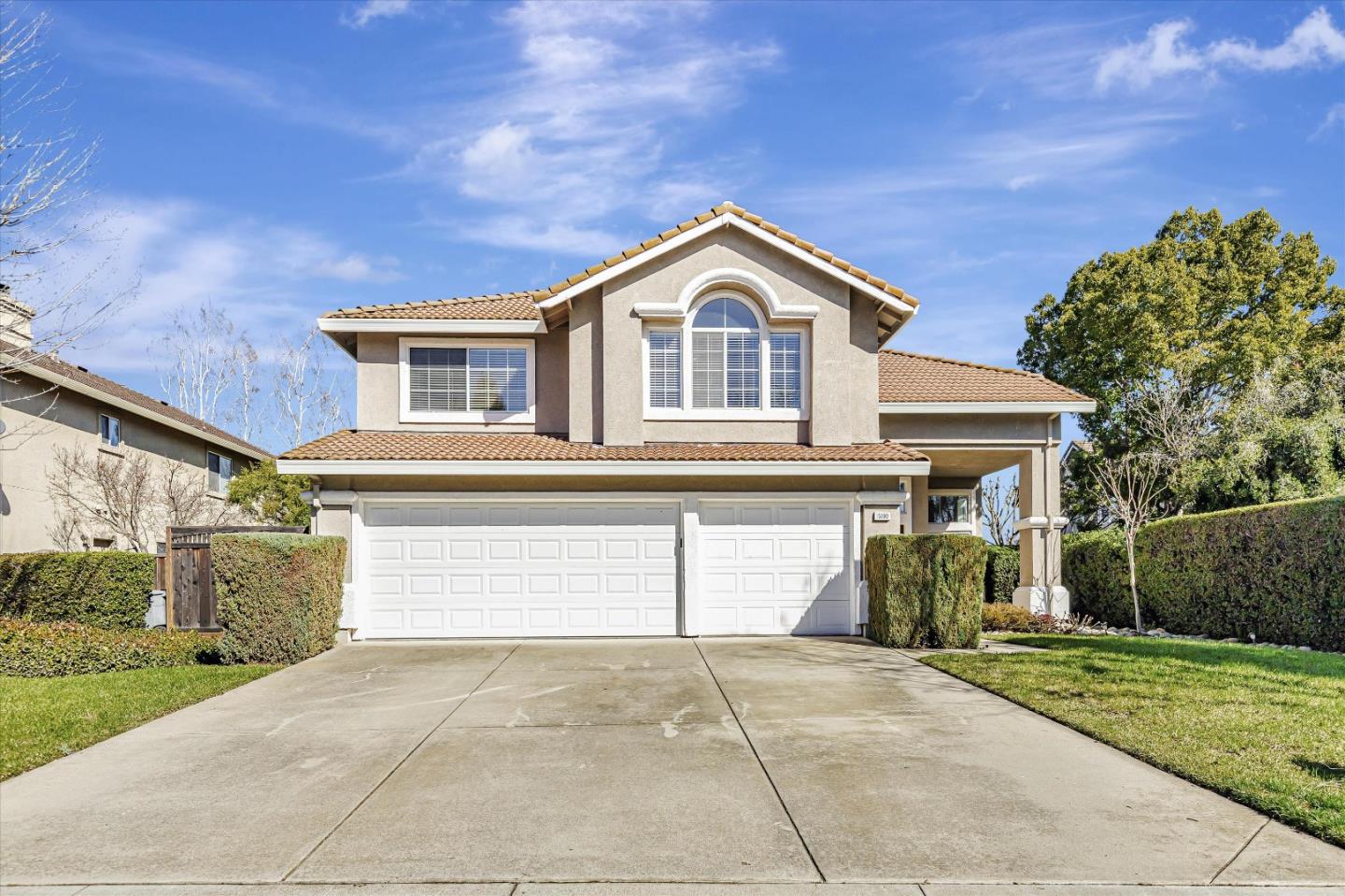 Two-story stucco home with a tile roof, arched window, and wide two-car garage.