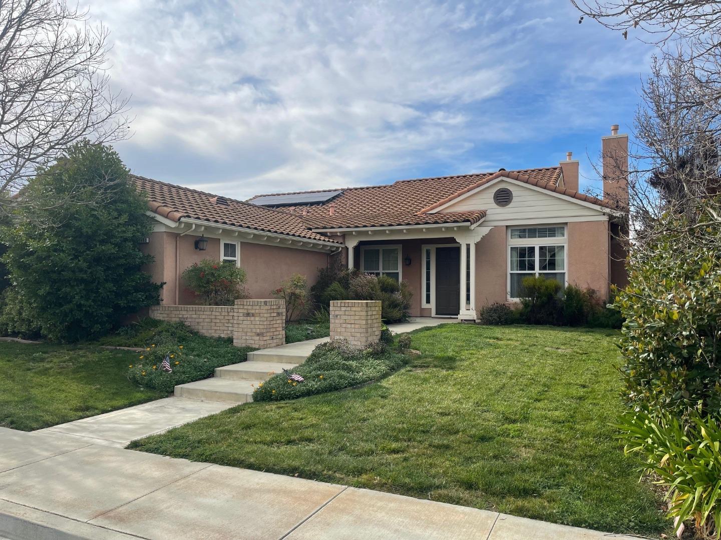 Single-story stucco home with a terracotta tile roof, solar panels, and a front lawn.
