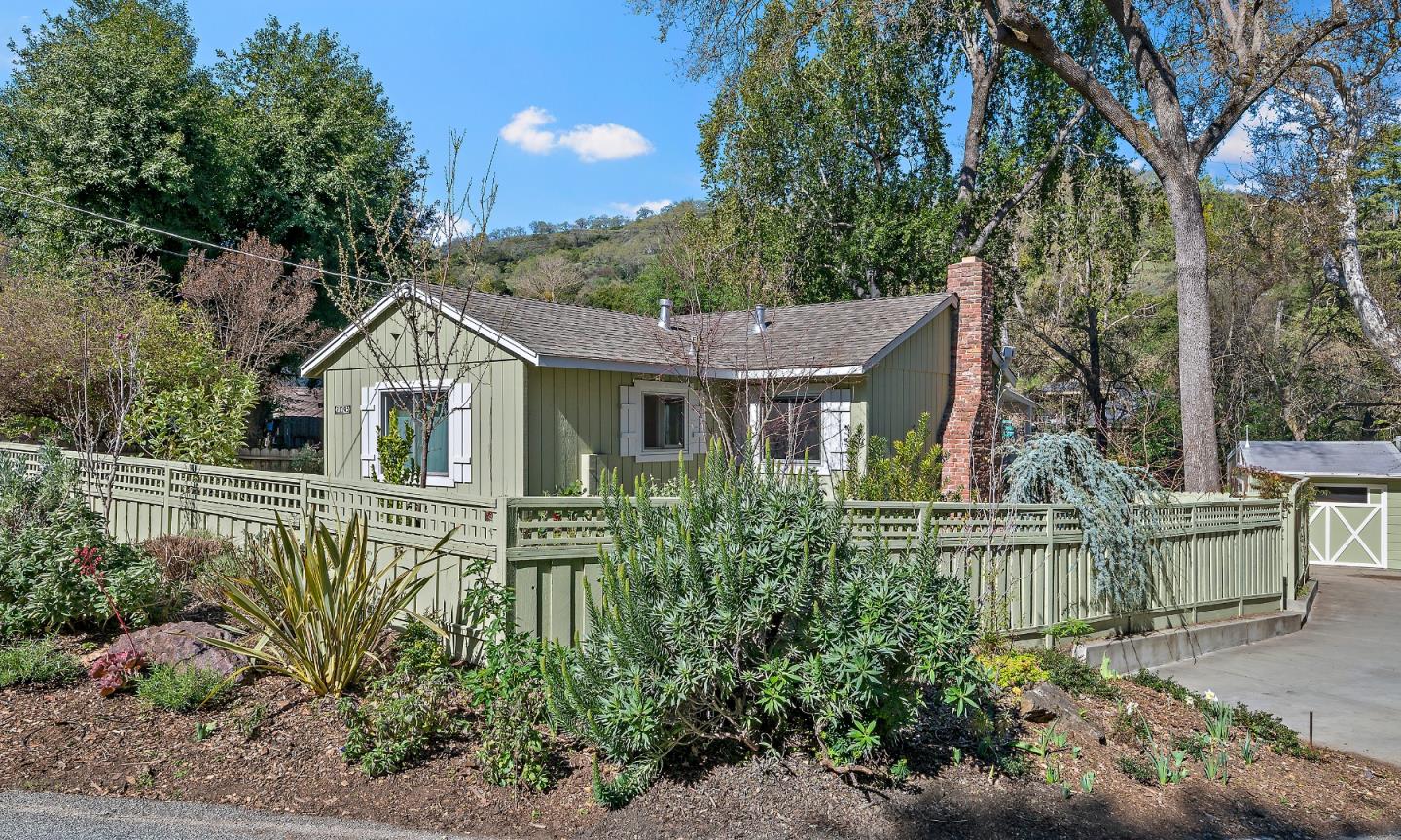 Single-story green house with white shutters, a brick chimney, and a landscaped fenced yard.