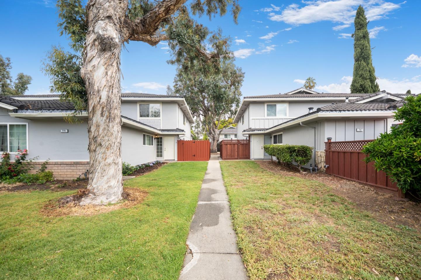 Attached homes flank a central walkway bordered by lawns, red wooden gates, and mature trees.