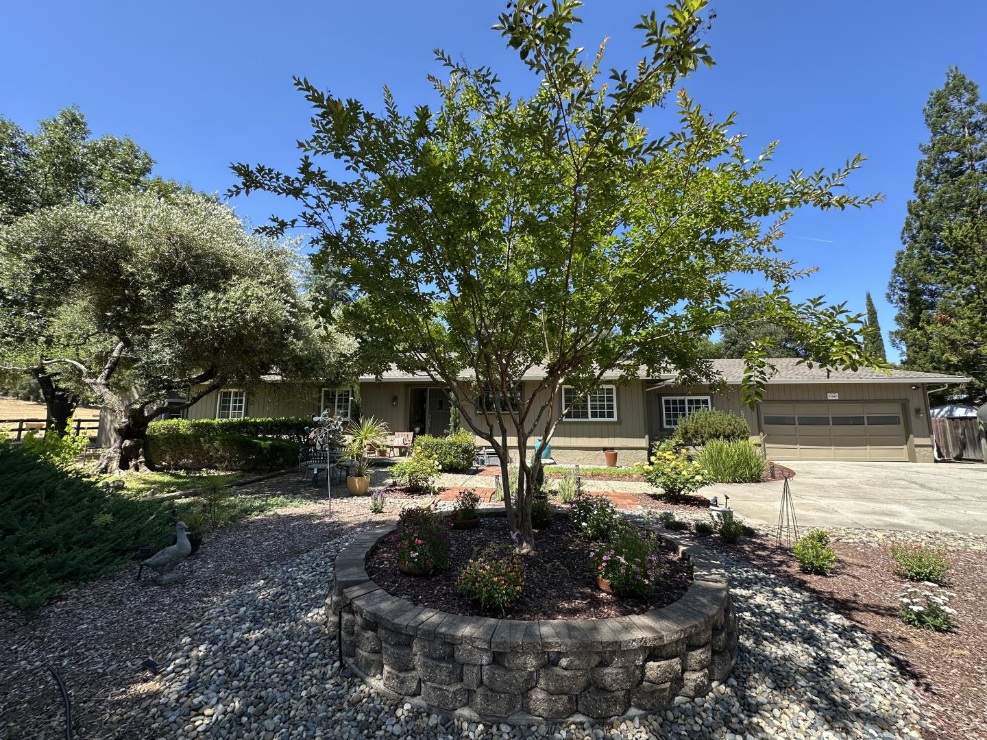 Single-story home with an attached garage behind a circular stone planter and landscaped front yard.
