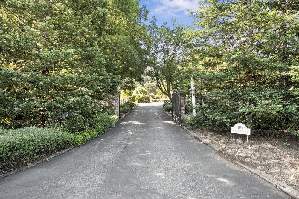 Tree-lined driveway entrance with an open gate and a sign for 1090 W Edmundson Ave.