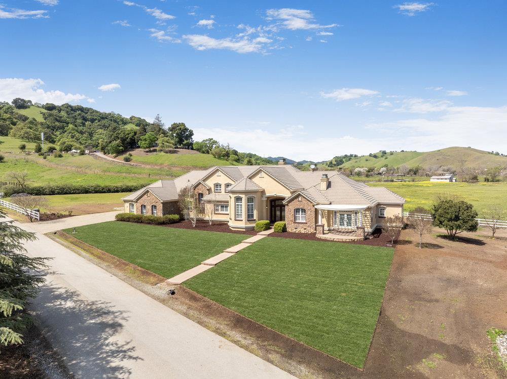 Large stone-and-stucco home with a broad green lawn, surrounded by rolling hills and open fields.