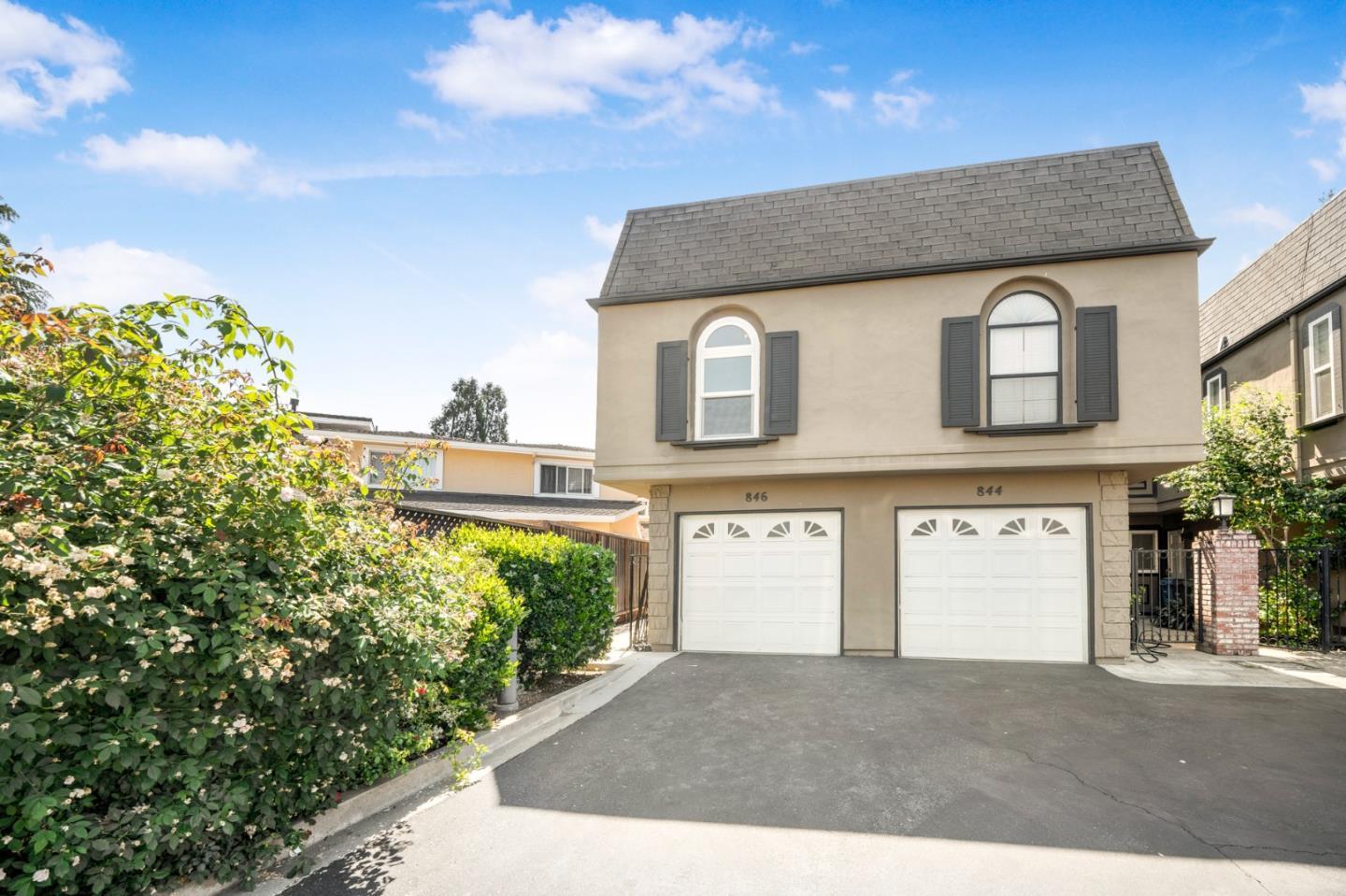 Beige two-story home with arched windows, twin garage doors, and leafy landscaping.