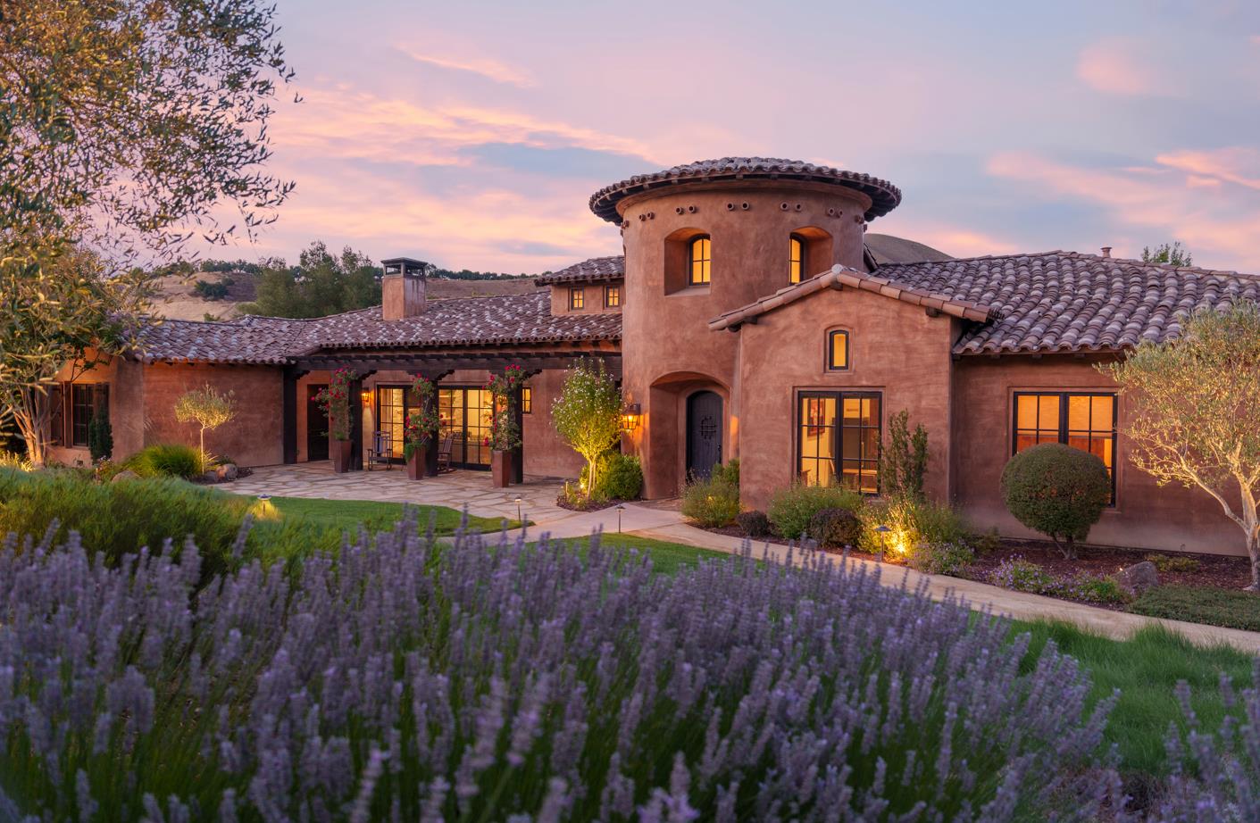 Spanish-style home with a round tower and tiled roof, framed by lavender at dusk.