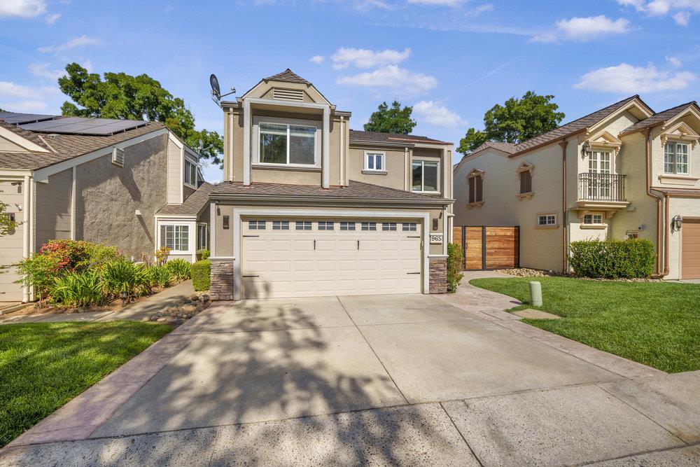 Two-story beige home with a double garage, broad driveway, and landscaped front lawn.