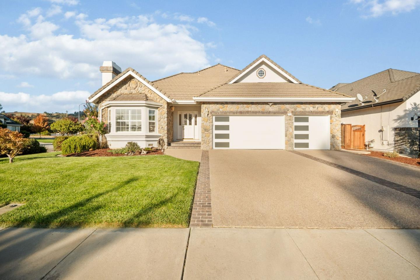 Stone-front home with two garage doors, a broad driveway, and a green front lawn.
